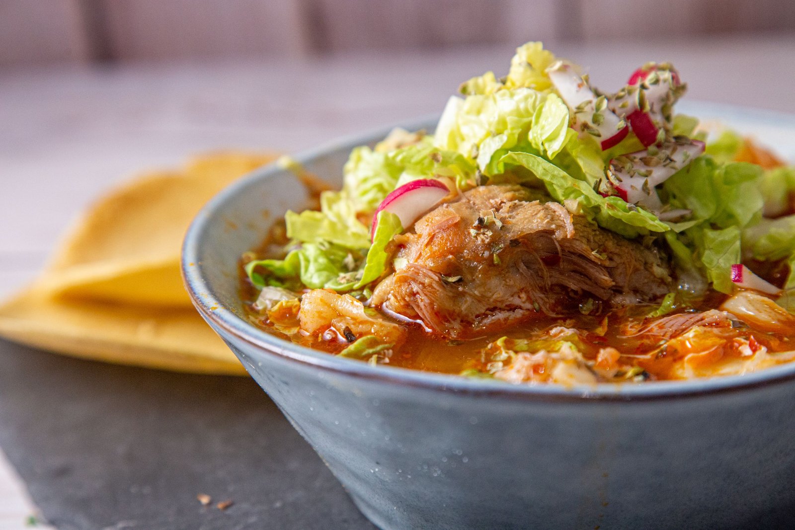 A bowl of red pozole topped with lettuce and sliced radishes